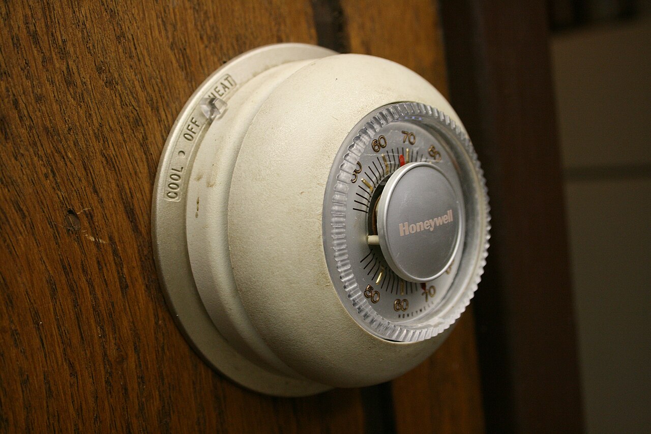 A round Honeywell thermostat on a wood wall, set between cool, off, and heat